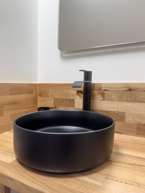 Musluk, yan görüş siyah seramik lavabo tahta tezgahta, aynanın altında. Modern banyo içi siyah seramik lavabo ve musluk musluğu var. banyo içi. 