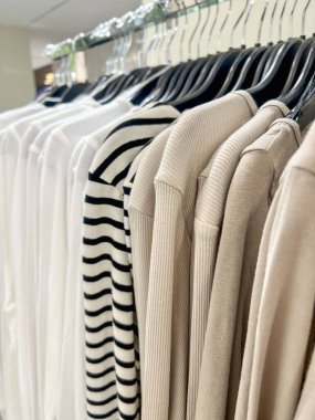 Neatly arranged beige, white, striped shirts on black hangers in store. fashion display in boutique. organized clothing rack with neutral tones, stylish apparel retail interior. department store background 