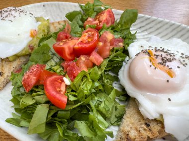 Kahvaltı, yanında çiğ yumurta, avokado tostu, yapraklı yeşil salata, doğranmış domates seramik tabakta servis edilen sağlıklı kahvaltı. Sağlıklı gıda konsepti 