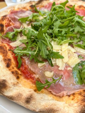 Italian pizza with parma ham prosciutto and arugula. Delicious closeup pizza with prosciutto or parma ham, arugula or rocket salad and parmesan on table. Italian food or cuisine background or surface