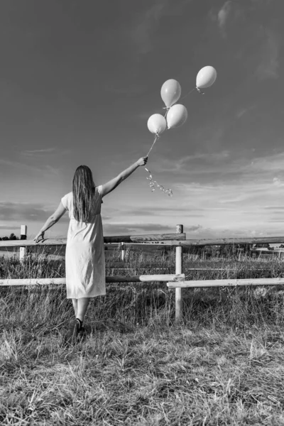 畑の真ん中の柵のそばに風船を持った女性が立っている — ストック写真