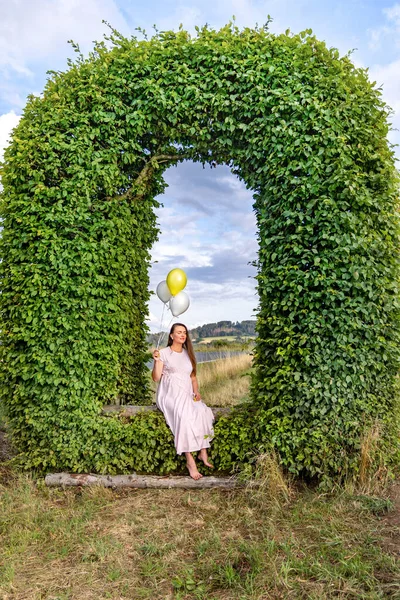 Eine Schwangere Frau Mit Luftballons Sitzt Einem Bogen Aus Grünen — Stockfoto