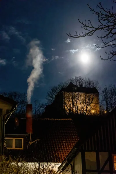 Moonlit night in an old German town, cloudy sky and full moon, smoke comes from the chimney