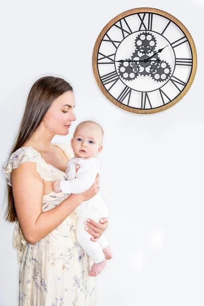Mama Trzyma Dziecko Ramionach Białej Ścianie Zegarem — Zdjęcie stockowe