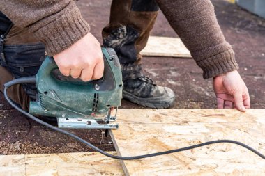 Marangoz elektrikli testereyle bir OSB tahtasını keser. Yapboz tam olarak keser.