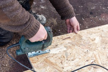 Marangoz elektrikli testereyle bir OSB tahtasını keser. Yapboz tam olarak keser.