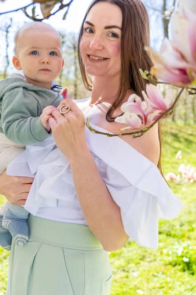 Kobieta Trzyma Syna Ramionach Pobliżu Kwitnącej Magnolii — Zdjęcie stockowe