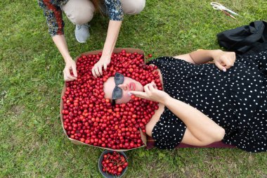 Sahne arkasında kirazlı genç bir kadını çekerken bir asistan karton kutuyu dutlarla dolduruyor.