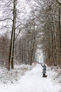 Karlı bir kış ormanında küçük bir köpeği olan bir kadın.
