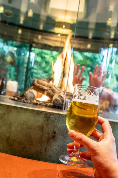 A hand holding a glass of beer against the background of a burning fire in a pub