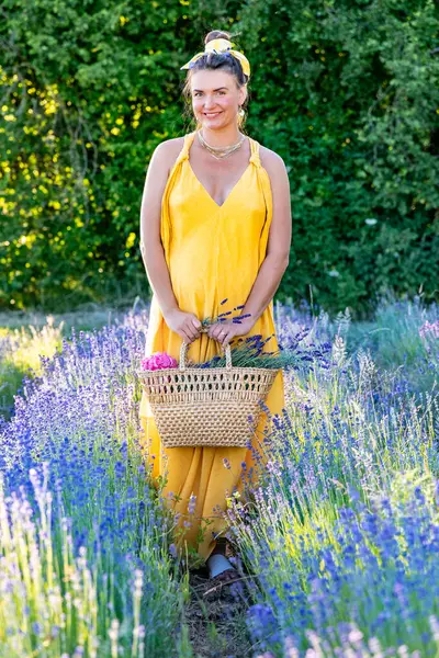 A happy woman in a yellow dress is standing on a blooming lavender field