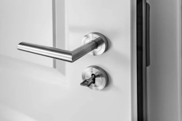 ラッチハンドルとキーホールの鍵付きのわずかに開いた白い木製のドアのクローズアップ ロイヤリティフリーのストック画像