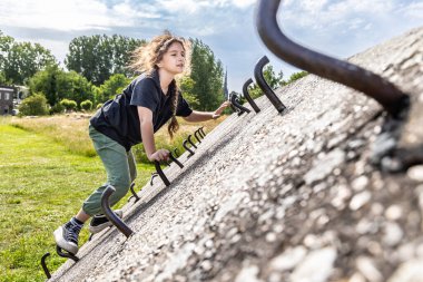 Bir kız beton duvara tırmanıyor, dışarıdaki bir duvara tırmanıyor.