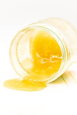 Beyaz arka planda bir kavanozdan bal dökülüyor, yakın plan.