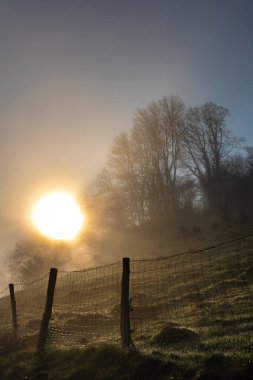 Sisli bir sabahta gün doğumu, güzel bir manzara, ön planda tel örgü.