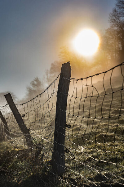 Sunrise on a foggy morning, beautiful landscape, wire fence in the foreground