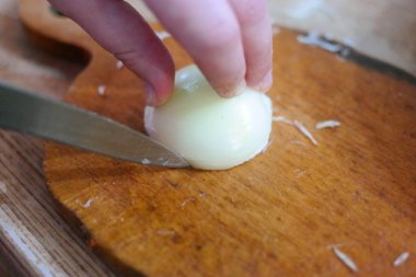 Soğan doğrama. Ahşap tahtanın soğanını bıçakla kesen şefin elleri. Yemek hazırlığı. Sağlıklı beslenme ve yaşam tarzı. Adam beyaz soğanı bıçakla kesiyor. Ev mutfağı. Yemek pişirme.