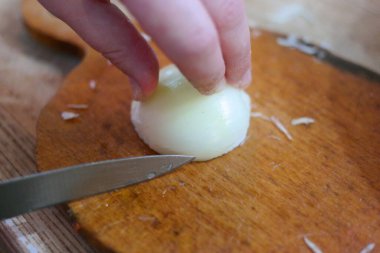 Soğan doğrama. Ahşap tahtanın soğanını bıçakla kesen şefin elleri. Yemek hazırlığı. Sağlıklı beslenme ve yaşam tarzı. Adam beyaz soğanı bıçakla kesiyor. Ev mutfağı. Yemek pişirme.