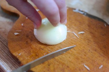 Soğan doğrama. Ahşap tahtanın soğanını bıçakla kesen şefin elleri. Yemek hazırlığı. Sağlıklı beslenme ve yaşam tarzı. Adam beyaz soğanı bıçakla kesiyor. Ev mutfağı. Yemek pişirme.