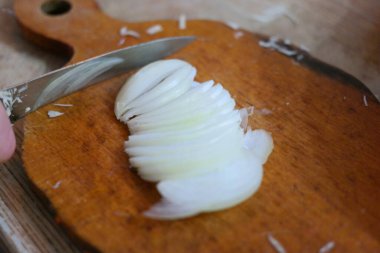 Soğan doğrama. Ahşap tahtanın soğanını bıçakla kesen şefin elleri. Yemek hazırlığı. Sağlıklı beslenme ve yaşam tarzı. Adam beyaz soğanı bıçakla kesiyor. Ev mutfağı. Yemek pişirme.