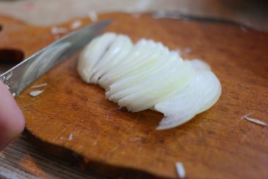 Soğan doğrama. Ahşap tahtanın soğanını bıçakla kesen şefin elleri. Yemek hazırlığı. Sağlıklı beslenme ve yaşam tarzı. Adam beyaz soğanı bıçakla kesiyor. Ev mutfağı. Yemek pişirme.