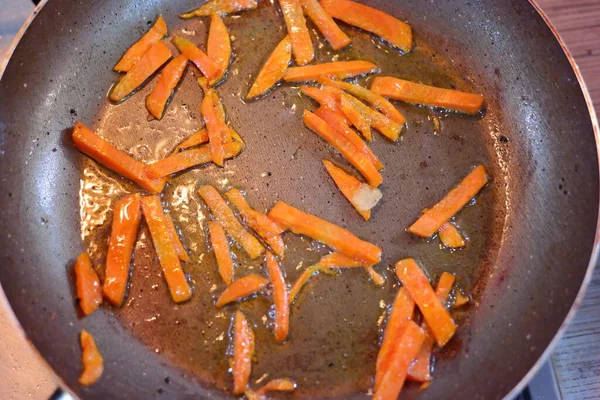 cutting carrots into slices. fried carrots in a pan. Sliced carrots and onions in a wok pan. Raw carrot strips in a pan with olive oil. prepared for frying. Carrot strips or julienne with onions