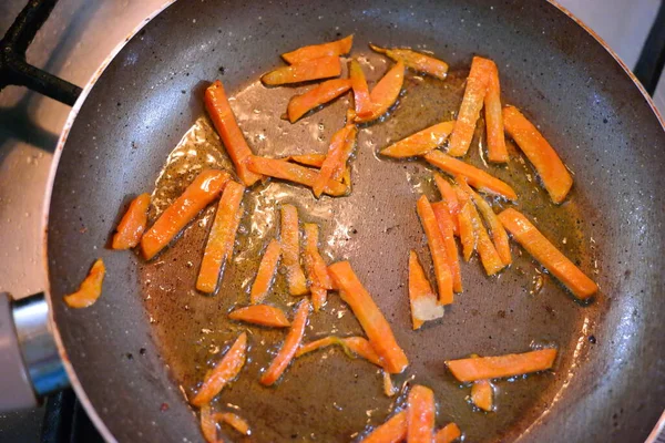 cutting carrots into slices. fried carrots in a pan. Sliced carrots and onions in a wok pan. Raw carrot strips in a pan with olive oil. prepared for frying. Carrot strips or julienne with onions