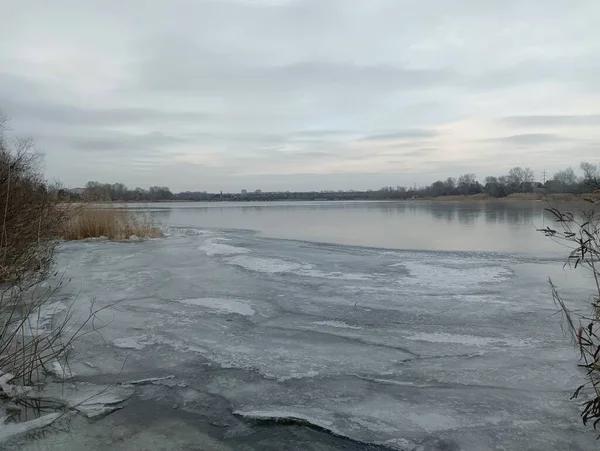 stock image ice on the river. frozen river. natural landscape with river in winter. Winter river bank with frozen water and branches under the snow on the shore.Cloudy weather.There is snow on the shore and low bushes grow.