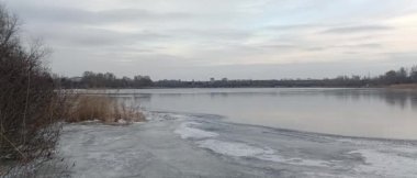 Nehirdeki buz. Donmuş nehir. Kışın nehirle birlikte doğal manzara. Kıyıda donmuş su ve dallarla kışın nehir kıyısında. Bulutlu hava. Kıyıda kar var ve alçak çalılar büyüyor..