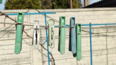 İpte çok renkli mandallar var. Tarafsız yeşil zeminde çiy damlaları olan mavi mandallar, beyaz telde mandallar, çamaşır ipi kurutma teli, çok renkli mandallar..