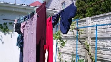 Giysiler iple kurumuş. Evin arka bahçesinde giysiler ve yatak örtüleri kuruyor, yakınlardaki çimlerin üzerinde bir çamaşır sepeti duruyor. Çamaşır yıkama sonrası kuruması için dışarıda beyaz çamaşır beyazları asılı.