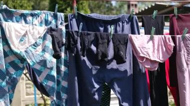 Giysiler iple kurumuş. Evin arka bahçesinde giysiler ve yatak örtüleri kuruyor, yakınlardaki çimlerin üzerinde bir çamaşır sepeti duruyor. Çamaşır yıkama sonrası kuruması için dışarıda beyaz çamaşır beyazları asılı.