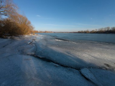 Nehirdeki buz. Donmuş nehirde yürü. Bir adam kar ve buz üzerinde yürür. Tehlikeli buz. dondurucu su. Buzda derin çatlaklar var. Nehirli güneşli kış manzarası. Kış nehri ve güneş.