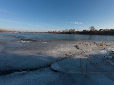 Nehirdeki buz. Donmuş nehirde yürü. Bir adam kar ve buz üzerinde yürür. Tehlikeli buz. dondurucu su. Buzda derin çatlaklar var. Nehirli güneşli kış manzarası. Kış nehri ve güneş.