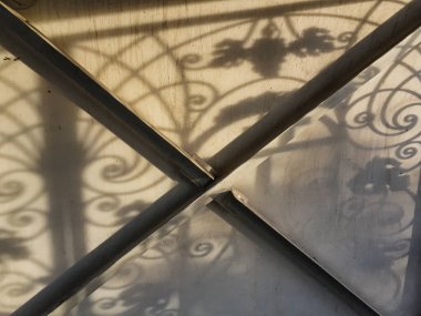 Duvardaki güzel gölgeler. Açık iş gölgeleri. Şehirde günbatımı. Demir ızgaraların ve beyaz duvardaki ağaçların uzun gölgeleri, yıpranmış duvar arka planının beyaz dokusuna doğal gölgeler örtülür..