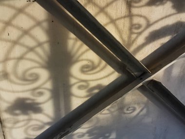 Duvardaki güzel gölgeler. Açık iş gölgeleri. Şehirde günbatımı. Demir ızgaraların ve beyaz duvardaki ağaçların uzun gölgeleri, yıpranmış duvar arka planının beyaz dokusuna doğal gölgeler örtülür..