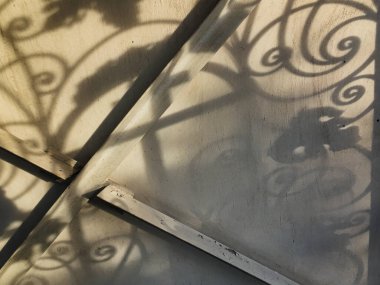 Duvardaki güzel gölgeler. Açık iş gölgeleri. Şehirde günbatımı. Demir ızgaraların ve beyaz duvardaki ağaçların uzun gölgeleri, yıpranmış duvar arka planının beyaz dokusuna doğal gölgeler örtülür..