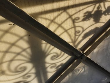 Duvardaki güzel gölgeler. Açık iş gölgeleri. Şehirde günbatımı. Demir ızgaraların ve beyaz duvardaki ağaçların uzun gölgeleri, yıpranmış duvar arka planının beyaz dokusuna doğal gölgeler örtülür..