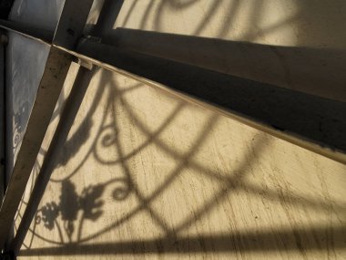 Duvardaki güzel gölgeler. Açık iş gölgeleri. Şehirde günbatımı. Demir ızgaraların ve beyaz duvardaki ağaçların uzun gölgeleri, yıpranmış duvar arka planının beyaz dokusuna doğal gölgeler örtülür..