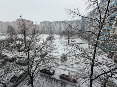 Karda çok katlı binalar. Şehirde kış mevsimi. Mahalledeki yüksek binaların yakınında kar yağışı var. Karda bir metropol. Büyük bir şehirde karlı bir kış manzarası.