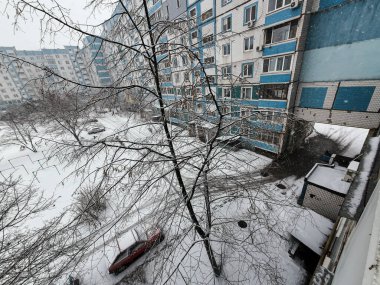 Karda çok katlı binalar. Şehirde kış mevsimi. Mahalledeki yüksek binaların yakınında kar yağışı var. Karda bir metropol. Büyük bir şehirde karlı bir kış manzarası.
