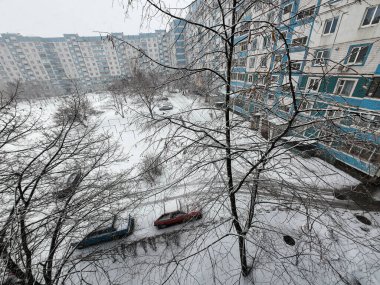 Karda çok katlı binalar. Şehirde kış mevsimi. Mahalledeki yüksek binaların yakınında kar yağışı var. Karda bir metropol. Büyük bir şehirde karlı bir kış manzarası.