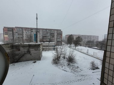 Karda çok katlı binalar. Şehirde kış mevsimi. Mahalledeki yüksek binaların yakınında kar yağışı var. Karda bir metropol. Büyük bir şehirde karlı bir kış manzarası.