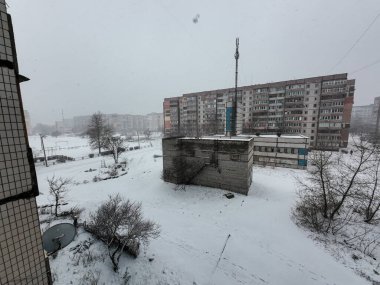 Karda çok katlı binalar. Şehirde kış mevsimi. Mahalledeki yüksek binaların yakınında kar yağışı var. Karda bir metropol. Büyük bir şehirde karlı bir kış manzarası.