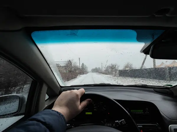 driver driving a car. bad road. potholes on the road. bad road conditions. POV person driving past another car during heavy snowfall along country road with winter trees aroun
