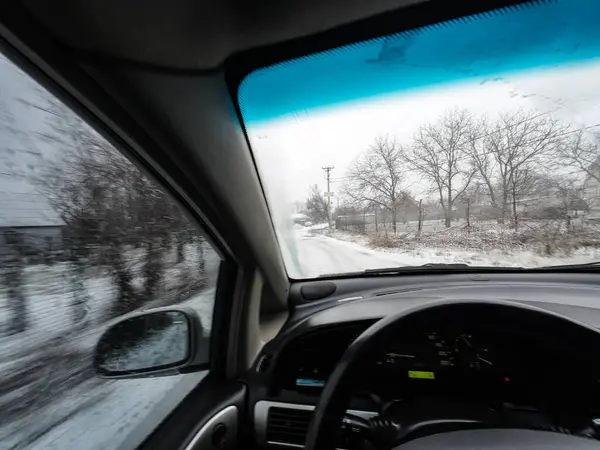 driver driving a car. bad road. potholes on the road. bad road conditions. POV person driving past another car during heavy snowfall along country road with winter trees aroun