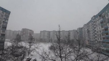 Karda çok katlı binalar. Şehirde kış mevsimi. Mahalledeki yüksek binaların yakınında kar yağışı var. Karda bir metropol. Büyük bir şehirde karlı bir kış manzarası.