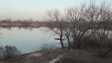 Nehirde akşam manzarası ve suda yansıması var. Renkli bulutlu gökyüzü ve ağaçlar sakin nehir suyuna yansıyor. Çimenler ve ağaçlar nehrin kıyısında yetişir. Evler suya yansıyor..