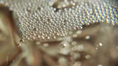 Kabarcıklar makro video. Şampanya köpükleri. Soyut şeffaf kabarcıkların ön görünümü sarı bir arkaplanda birleşiyor. Şampanya bardağındaki köpüklü baloncukların üst görüntüsü.