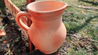 Antika kil sürahi. Ahşap bir çitin üzerindeki kil sürahi bahçedeki bir ağacın arka planına karşı. Kadim büyük kavanoz, içme suyu, su kaynağı, akan su, musluk suyu. Retro biçimi.